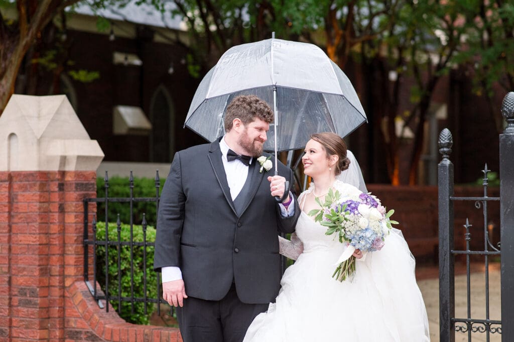 Bride and Groom holding an umbrella on their wedding day and not letting rain ruin their day.